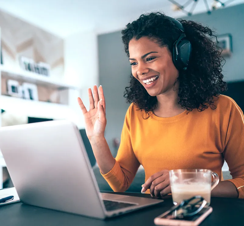 A woman smiles and waves during a video call.